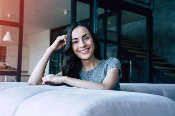 Portrait of smiling happy cute woman while sitting on the couch at home and relaxing - Fotografie, Obrázek