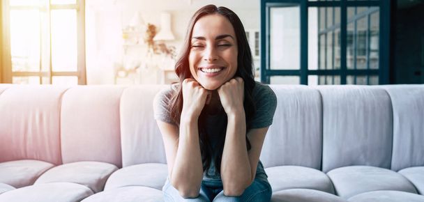 Portrait of smiling happy cute woman with closed eyes sitting on the couch at home - Photo, Image