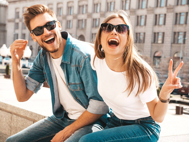 Portrait of smiling beautiful girl and her handsome boyfriend. Woman in casual summer jeans clothes. Happy cheerful family. Female having fun on the street background in sunglasses.Shows peace sign - Photo, Image