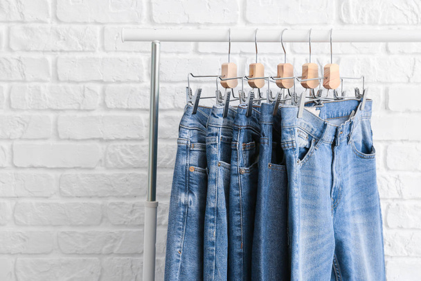 Стійка для одягу з різними стильними джинсовими штанами на білому цегляному фоні
 - Фото, зображення