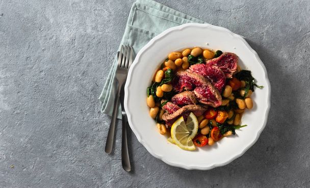 Dinner plate with beef steak, white beans, spinach and tomatoes top view with copy space - Fotoğraf, Görsel