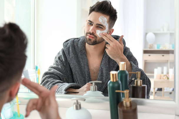 Bonito homem aplicando máscara de barro em seu rosto em casa
 - Foto, Imagem