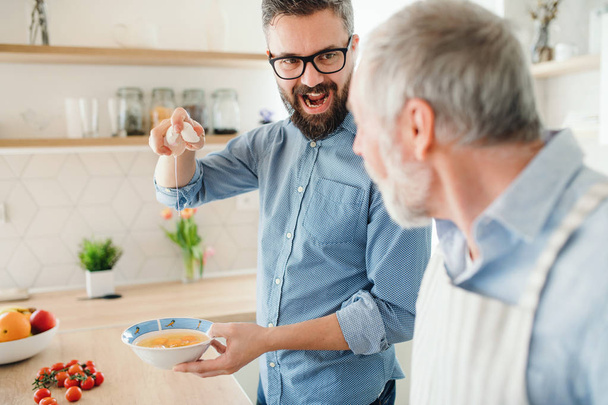 An adult hipster son and senior father indoors at home, cooking. - Foto, Bild