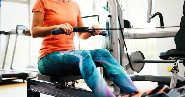 Woman pulling on row machine in fitness studio - Zdjęcie, obraz
