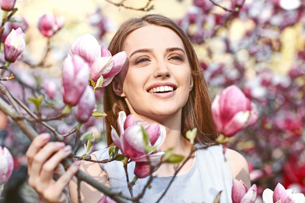 Portrait of beautiful young woman near blooming magnolia tree outdoors - 写真・画像