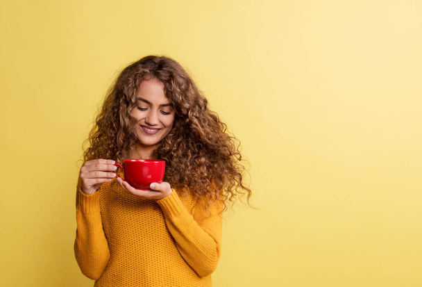 Portrait of a young woman with red cup in a studio on a yellow background. - Fotó, kép
