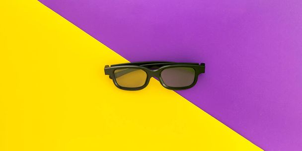 Gafas 3D negras, sobre divertido fondo amarillo púrpura vivo. Puesta plana
. - Foto, Imagen