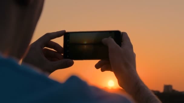 Hombre tomando fotos de la puesta del sol con smartphone en el muelle de la ciudad
 - Imágenes, Vídeo