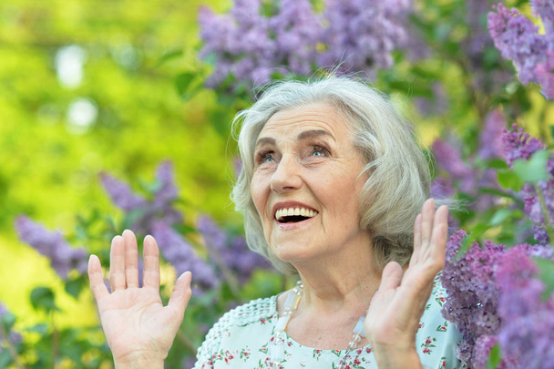 happy  senior beautiful woman on  lilacs background  in spring  park - Zdjęcie, obraz
