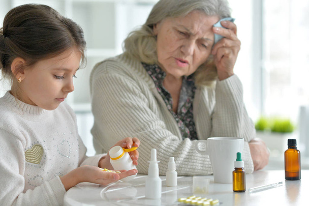 Cute girl giving medicine to sick senior woman - Фото, изображение