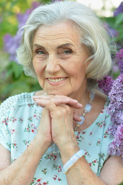 šťastná starší krásná žena na pozadí lilacsu v jarním parku - Fotografie, Obrázek