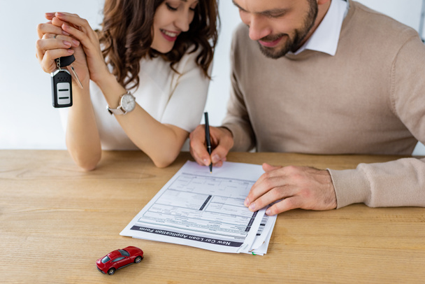 селективное фокусирование бородатого мужчины на подписании контракта рядом с женщиной, держащей ключ от машины
  - Фото, изображение