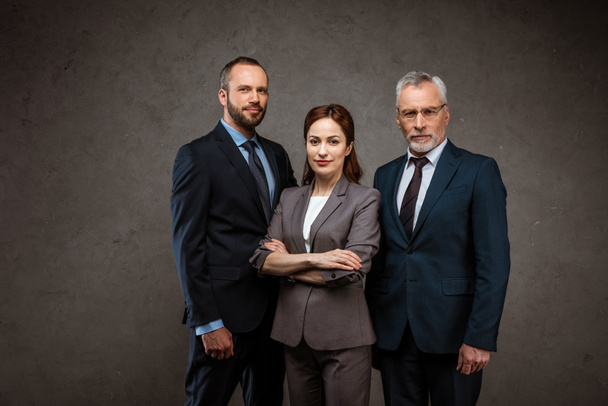 attractive businesswoman standing with crossed arms near men on grey - Фото, зображення