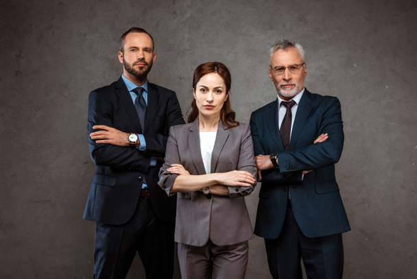 mulher de negócios atraente e homens de negócios bonitos de pé com braços cruzados em cinza
  - Foto, Imagem