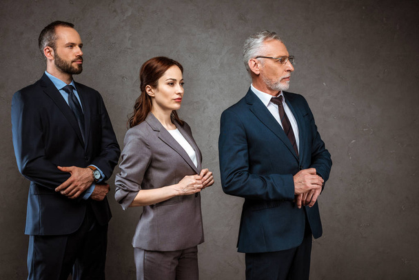 businessmen and attractive businesswoman standing in formal wear on grey  - Photo, Image