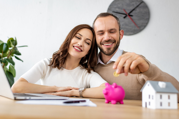 selective focus of happy man putting golden coin in pink piggy bank near attractive woman  - Photo, Image