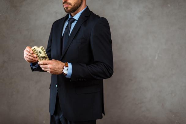 cropped view of bearded businessman holding dollar banknotes on grey  - Photo, Image