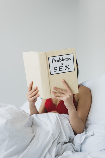 young woman in red bra reading problems in sex book while lying in bed - Zdjęcie, obraz
