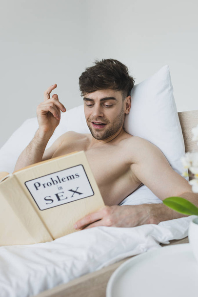 fröhlicher Mann zeigt Ideenschild beim Lesen von Problemen in Sexbuch  - Foto, Bild