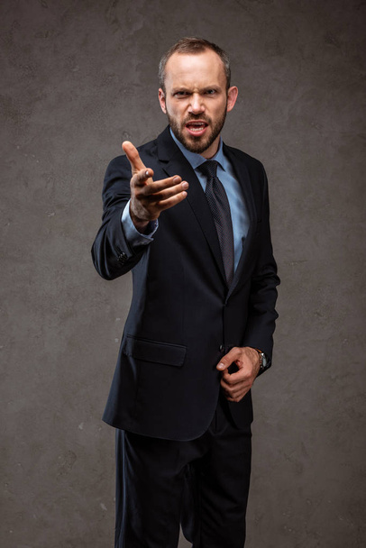 angry bearded businessman in suit gesturing on grey  - Фото, зображення