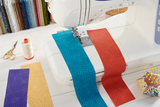 Sewing machine with a strips of fabrics on the background of stack of colorful quilting fabrics, sewing accessories - Φωτογραφία, εικόνα