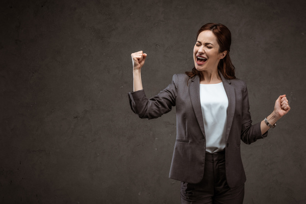 excited brunette woman celebrating triumph while standing on grey  - Photo, Image