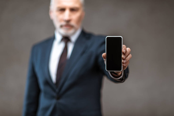 selective focus of businessman holding smartphone with blank screen on grey  - Fotografie, Obrázek