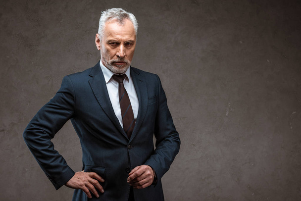 confident businessman in suit standing with hand on hip on grey  - Foto, Imagem