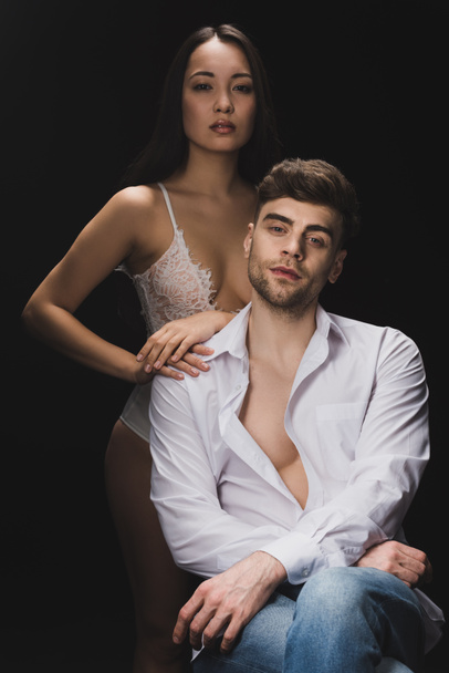 beautiful sexy asian woman in white lingerie standing near sitting boyfriend isolated on black - Fotó, kép