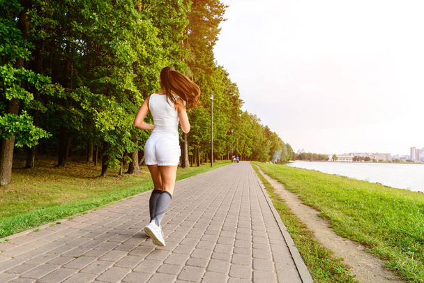 Beautiful female running on the bridge during everyday practice. Fitness woman jogging outdoors in park - Foto, afbeelding