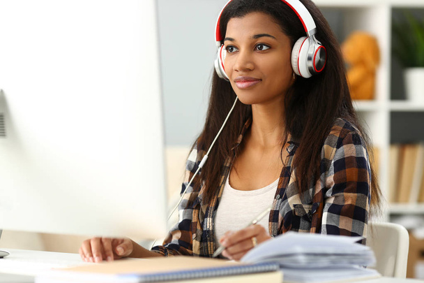 Black smiling woman sitting at workplace wearing headphones - Fotó, kép