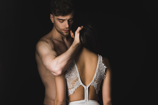 schöner Mann ohne Hemd umarmt sexy Freundin in weißen Dessous isoliert auf schwarz - Foto, Bild