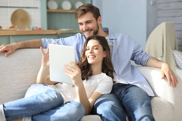 Young couple watching media content online in a tablet sitting on a sofa in the living room. - Fotografie, Obrázek