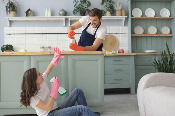 Young happy couple is having fun while doing cleaning at home. - Φωτογραφία, εικόνα