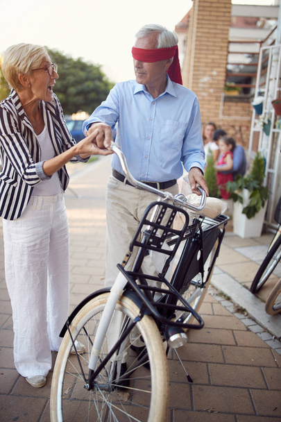 Senior vrouw bedekt ogen van senior man voor verrassing met het kopen - Foto, afbeelding