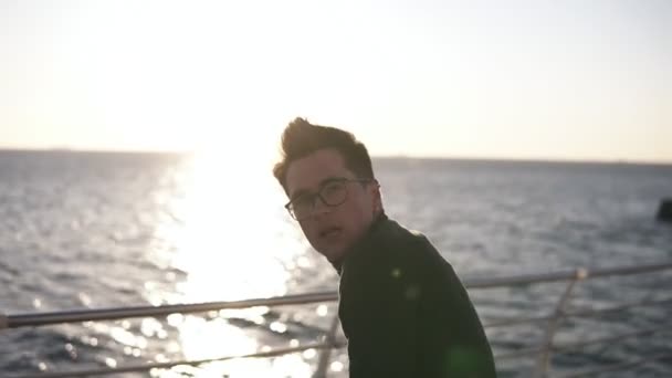 A young guy in a black blazer and glasses on the beach practiced dancing in the morning sun. Expesive dances outdoors. Slow motion - Video, Çekim