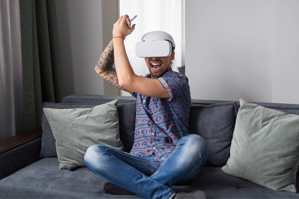 Excited guy playing action VR game at home - Foto, afbeelding