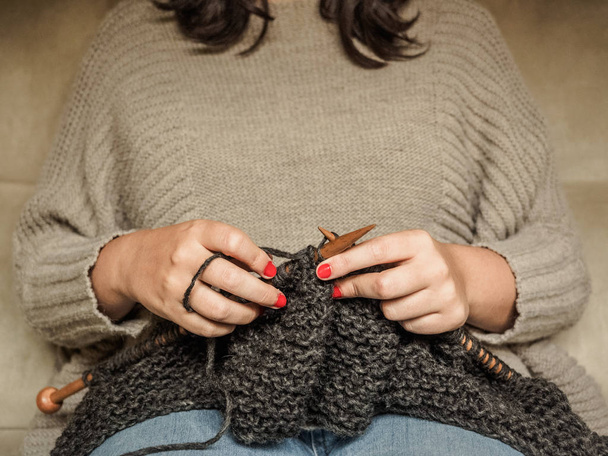 Meisje met rode nagels breien donkere grijze wol met houten naalden - Foto, afbeelding