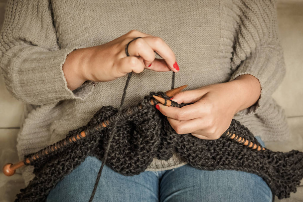 Girl with red nails knitting dark gray wool with wooden needles - Photo, Image