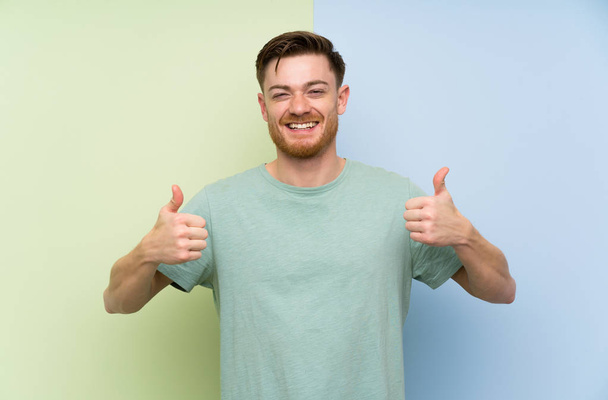 Redhead man over colorful background giving a thumbs up gesture - Photo, Image