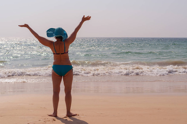 Счастливая пожилая женщина в шляпе с поднятыми руками на фоне моря на закате. Концепция солнечного и счастливого лета
. - Фото, изображение