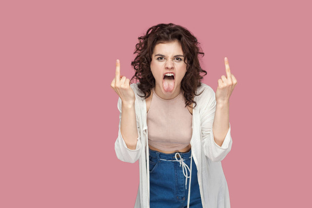 angry screaming brunette young woman with curly hairstyle in casual style looking at camera and showing middle finger fuck sings on pink background - Zdjęcie, obraz