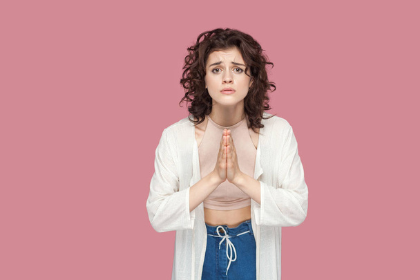 hopeful young woman with curly hairstyle in casual style standing with palm hands and looking at camera on pink background - Foto, Imagen