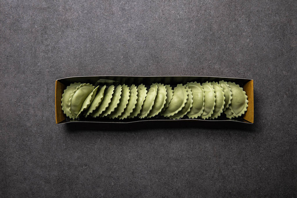 top view of green raw ravioli in cardboard box on grey textured surface - Photo, image