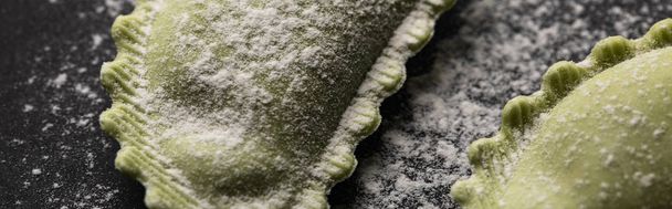 panoramic shot of green raw ravioli with flour on black table - Foto, Bild