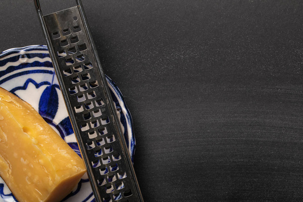 top view of sharp grater with cheese on ornate plate on black background - Valokuva, kuva