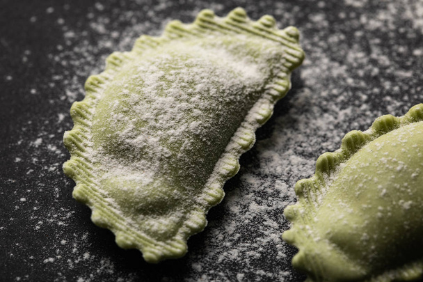 close up view of green fresh ravioli with flour on black surface - Foto, afbeelding