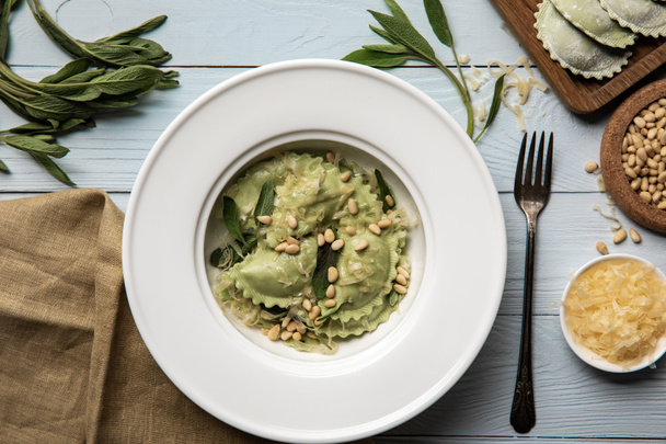 top view of green ravioli served in white plate with pine nuts, sage and grated cheese  - Fotoğraf, Görsel