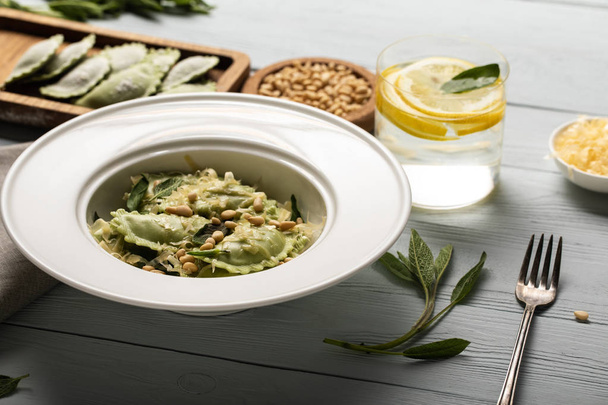 green ravioli with pine nuts, grated cheese and sage at wooden table near water with lemon - Φωτογραφία, εικόνα