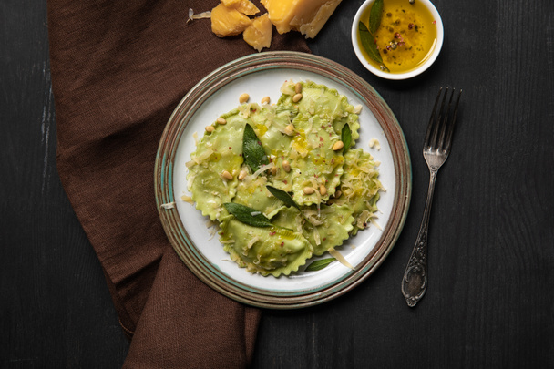 top view of green ravioli served in vintage plate near silver fork at black wooden table - 写真・画像